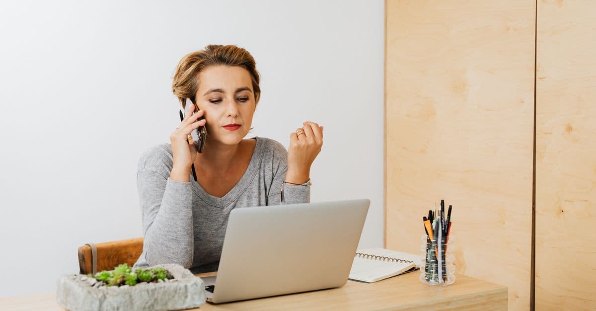 Fokussierte Frau arbeitet mit Laptop und Smartphone in modernem Arbeitsraum.