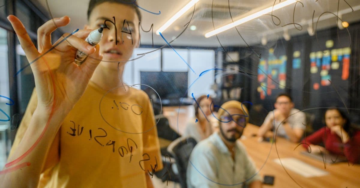 Team beim gemeinsamen Brainstorming an einer Glaswand in modernem Büro