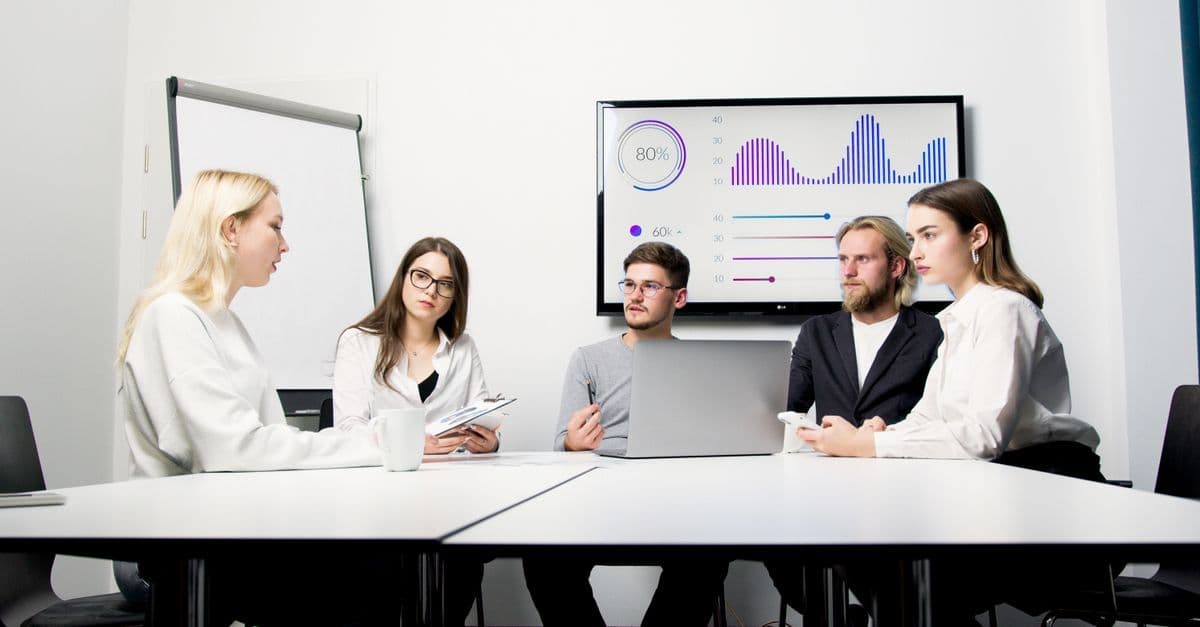 Mehrere Fachleute in einer Besprechung vor einer Datenpräsentation auf dem Bildschirm.