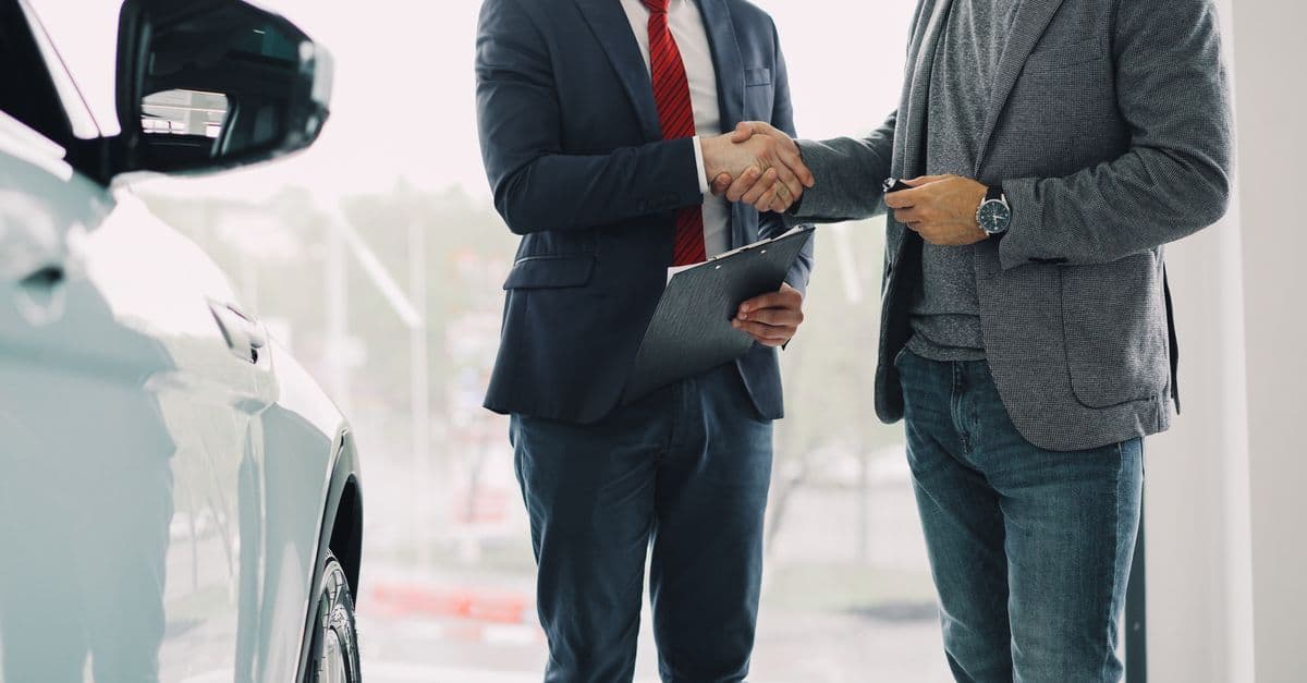 Zwei Männer geben sich im Autohaus die Hand neben einem Neuwagen.