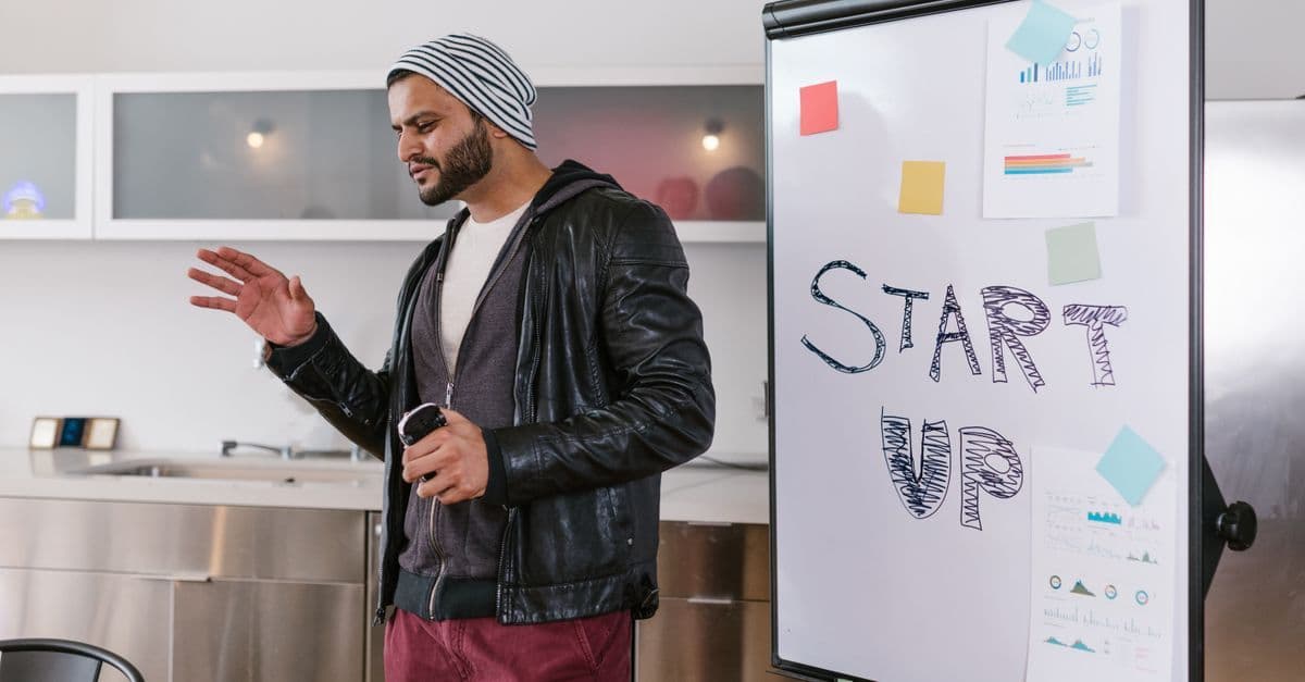 Bärtiger Mann präsentiert drinnen einen Startup-Geschäftsplan am Whiteboard.