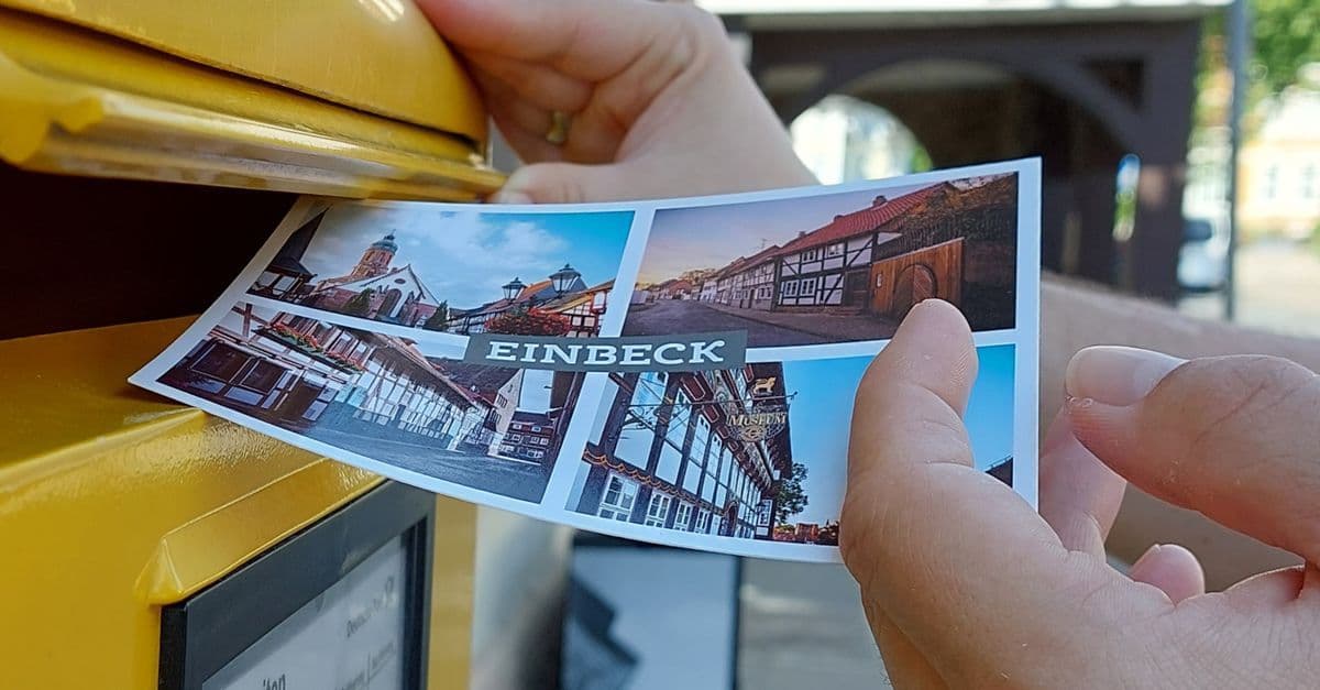 Close-up of a postcard being inserted into a yellow mailbox in Einbeck, Germany.