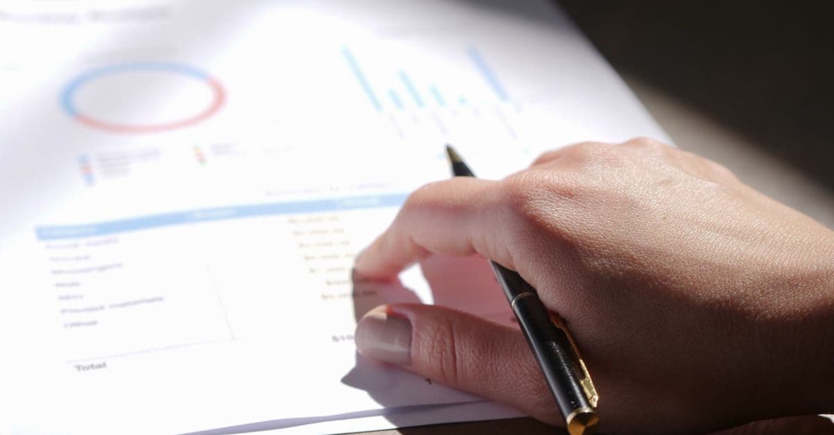 Hand mit Stift prüft Finanzdiagramme auf Papier im Nahaufnahmeformat