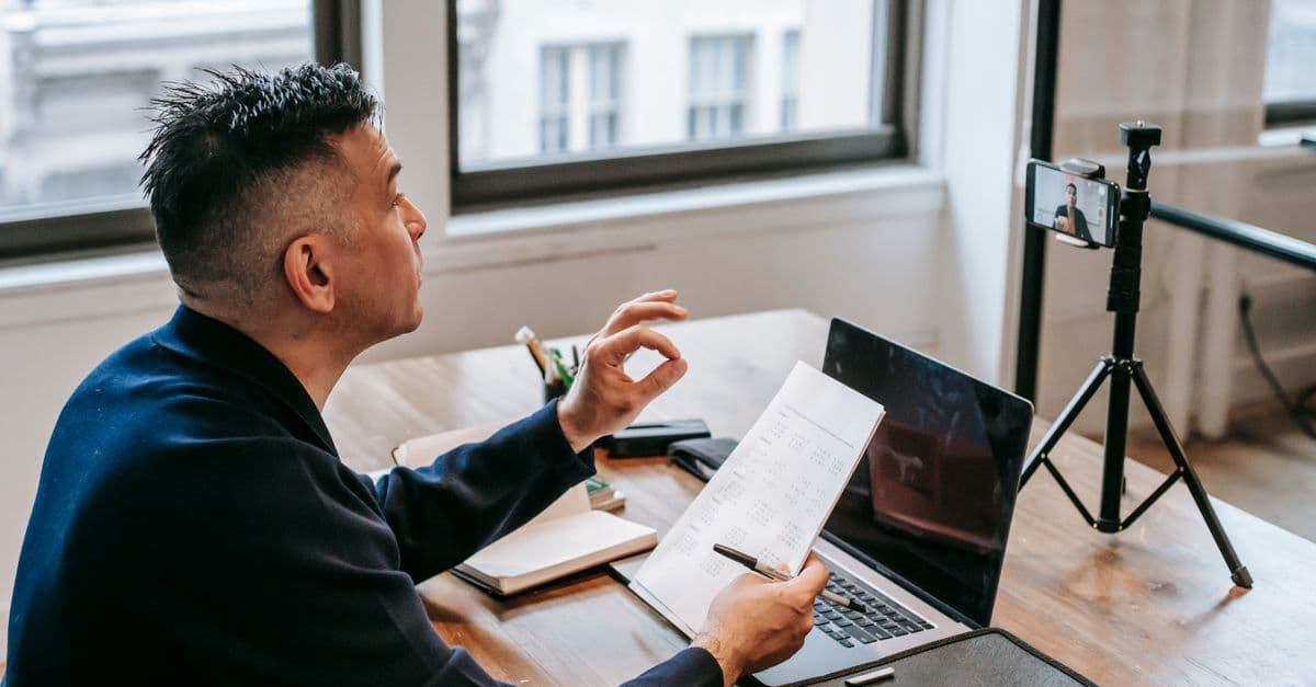 Mann im Büro mit Laptop und Smartphone während eines Videoanrufs
