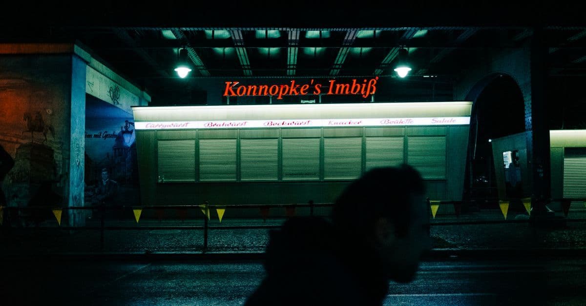 Mysterious night view of Konnopke's Imbiss in Berlin with silhouette foreground.