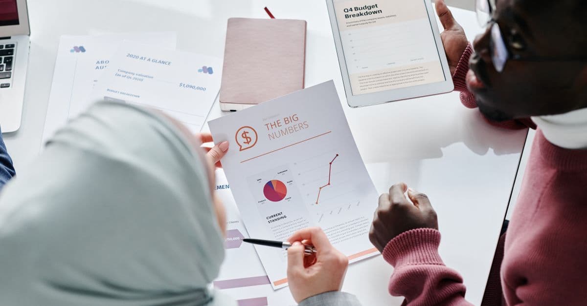 Zwei Kollegen prüfen Finanzunterlagen und Diagramme bei einer Besprechung im Büro.