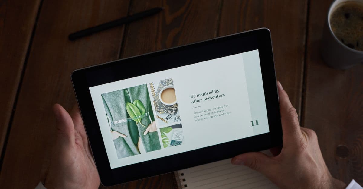 Hände halten ein Tablet mit geöffneter Präsentation über einem Holztisch.
