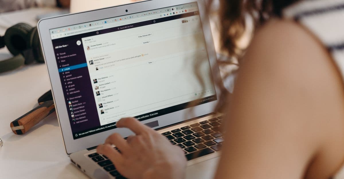 Geschäftsfrau tippt im Büro am Laptop und kommuniziert über Slack.