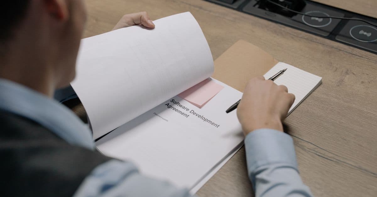 Business professional at the desk examining a software development agreement document.