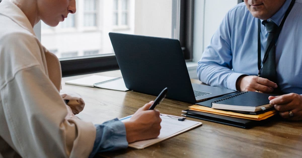 Gesichtslose Kollegen in Businesskleidung unterzeichnen am Tisch Dokumente neben Laptop und Ordner