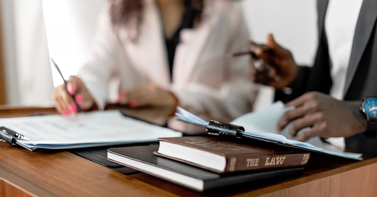 Zwei Anwälte prüfen Dokumente an einem Schreibtisch mit Gesetzbüchern in professioneller Umgebung.