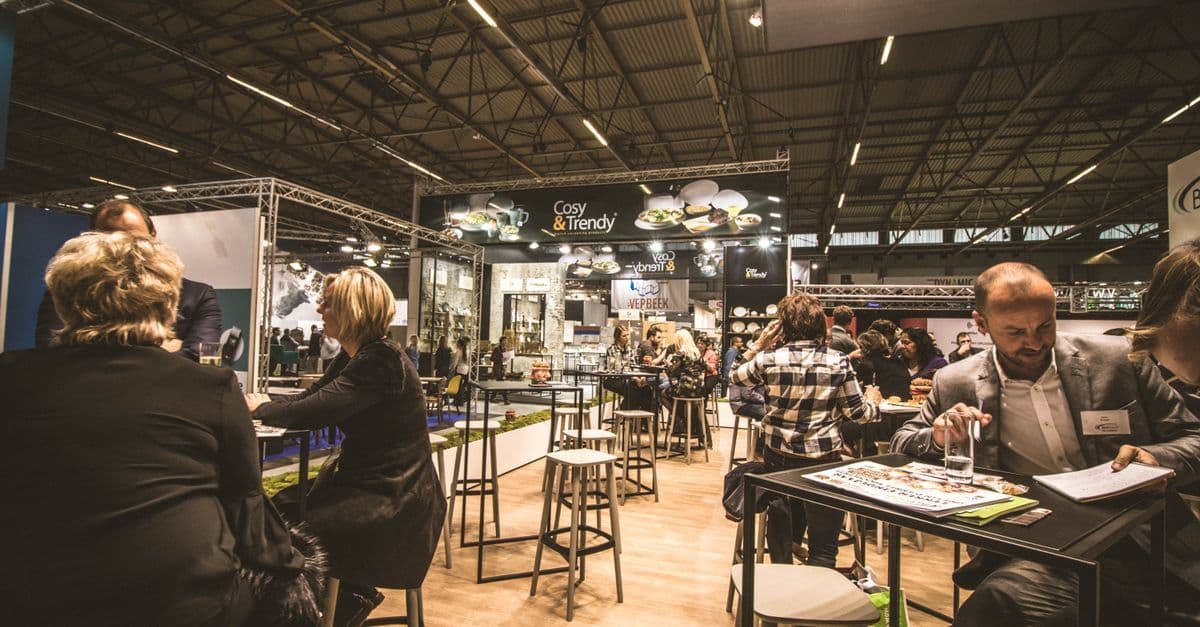 Geschäftsleute tauschen sich auf einer belebten Indoor-Messe an mehreren Ständen aus.