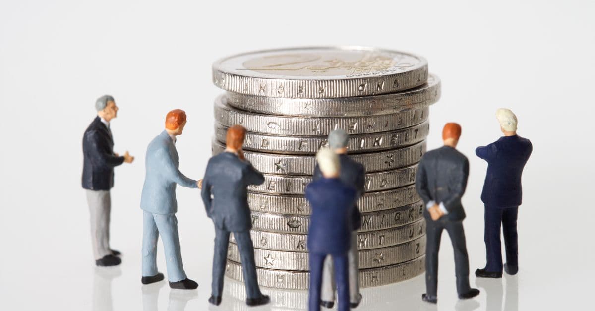 Miniature figurines of businessmen surround a stacked pile of coins on a clean white background.