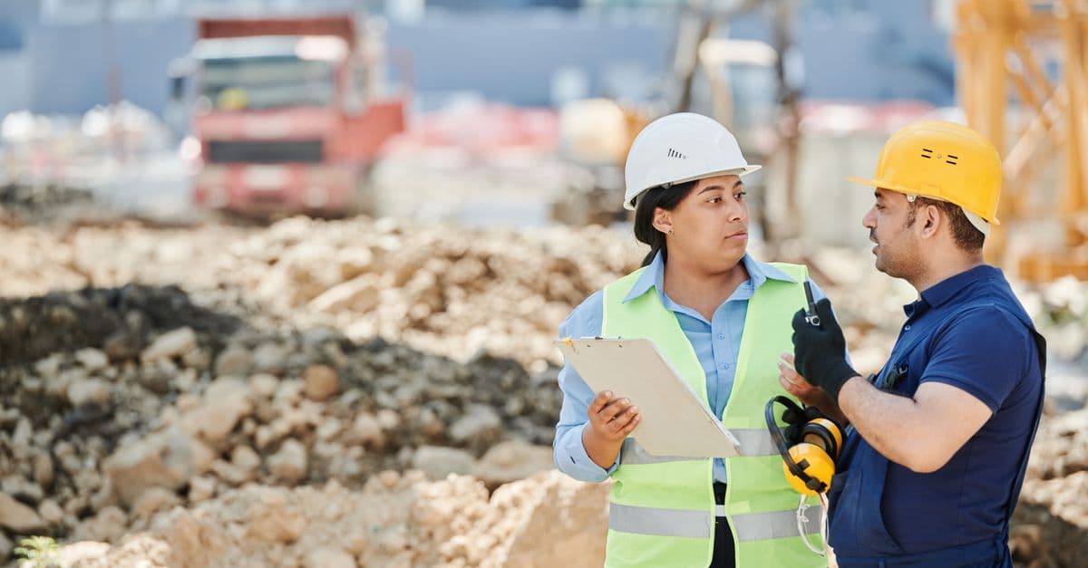 Zwei Bauarbeiter in Schutzkleidung besprechen Baupläne auf einer Baustelle.