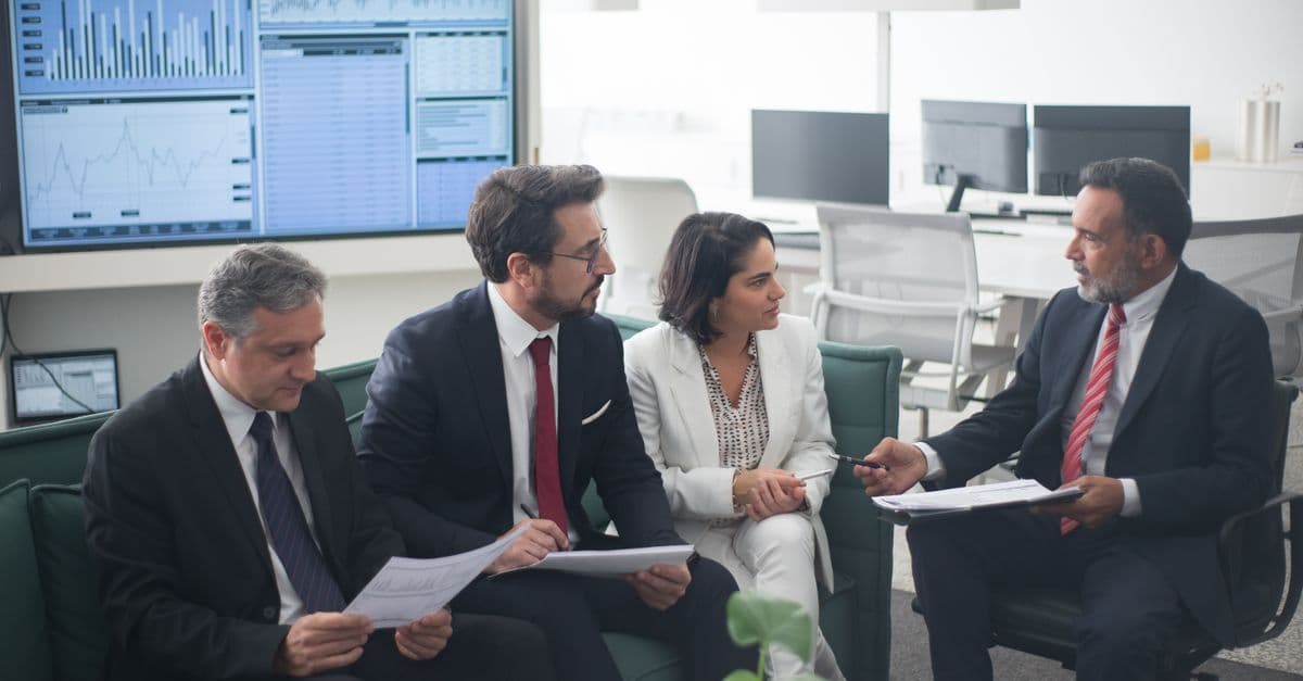 Mehrere Geschäftsleute besprechen Finanzstrategien in einem modernen Büro mit Unterlagen und Laptop.