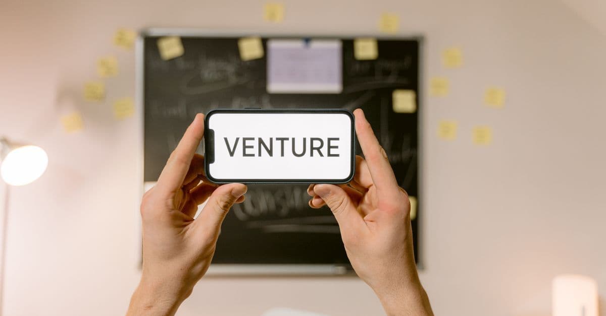 A smartphone displaying 'Venture' held by hands in an office setup. Ideal for business and startup themes.