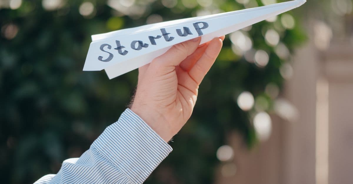 Close-up of a hand holding a paper plane with 'Startup' written, symbolizing a business launch.
