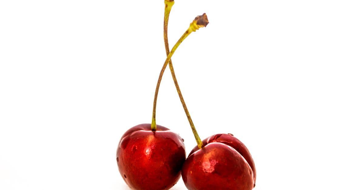 Close-up shot of two ripe red cherries with water droplets on a white background.