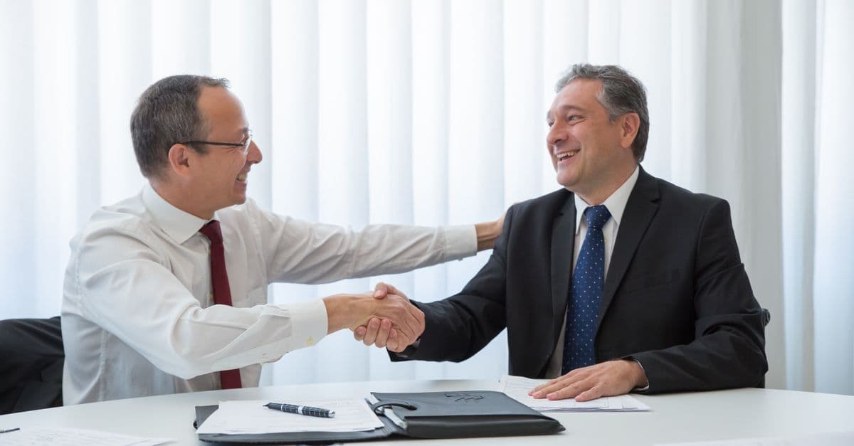 Two businessmen in a bright office seal a deal with a handshake, conveying agreement and cooperation.