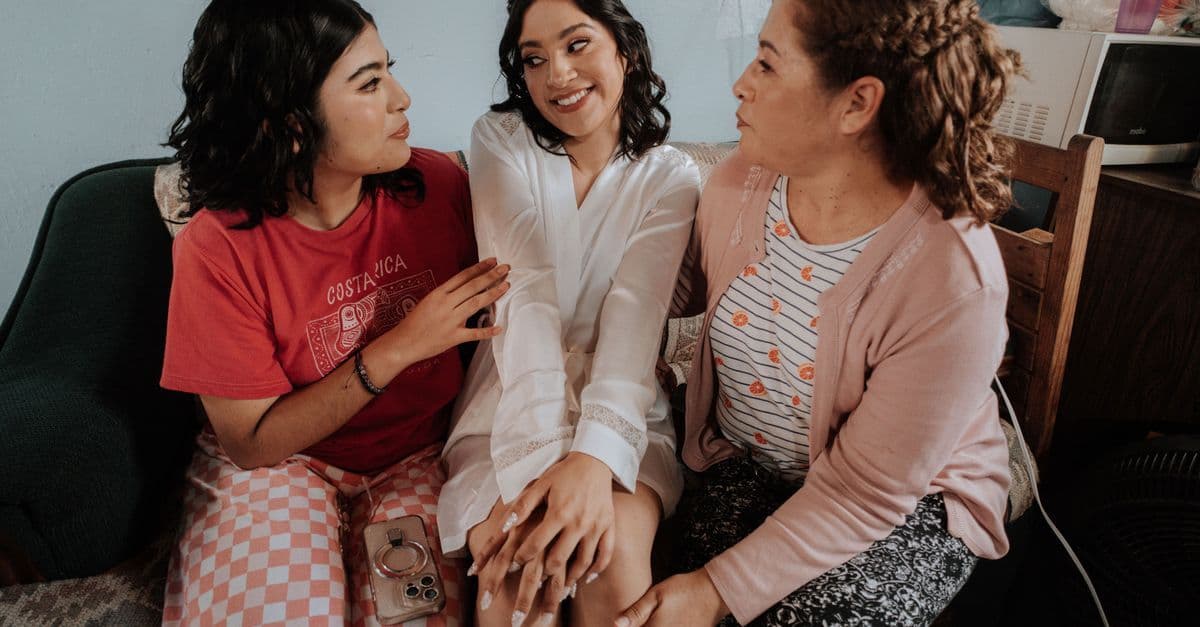 Three women sitting indoors sharing a joyful moment in a casual setting.