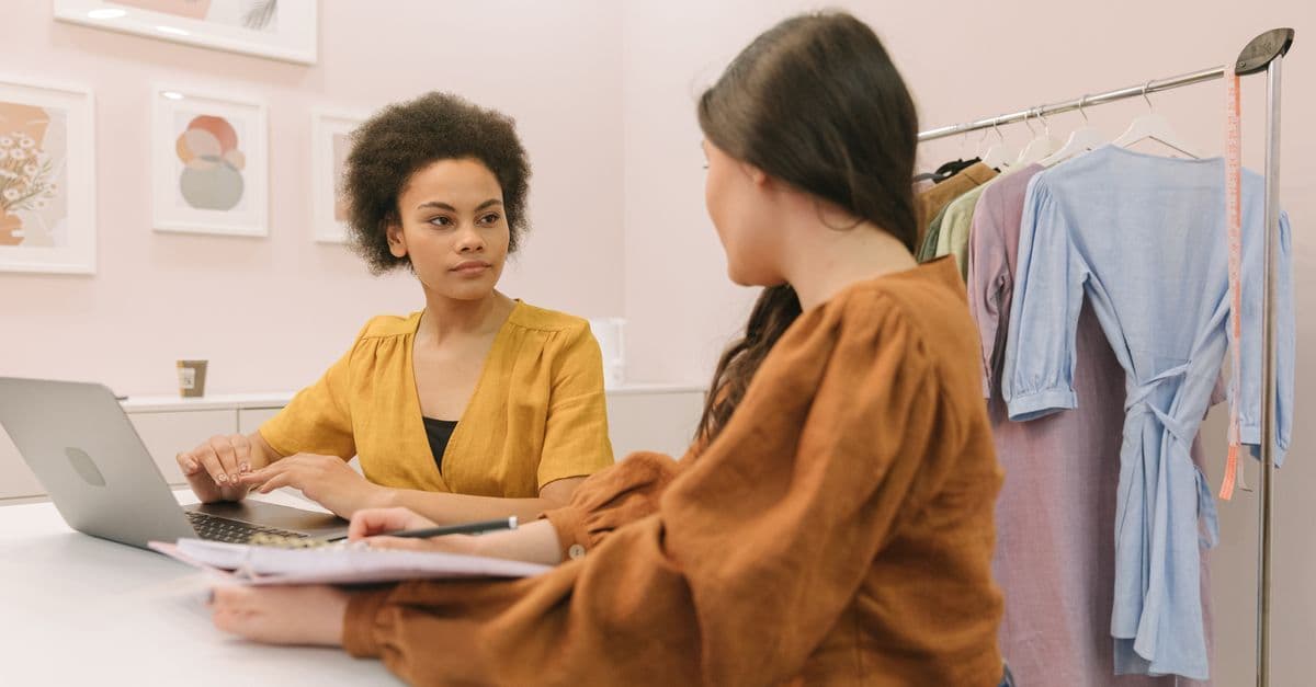 Zwei Frauen besprechen in einem Raum mit Kleiderständer eine Strategie für ein Modegeschäft.