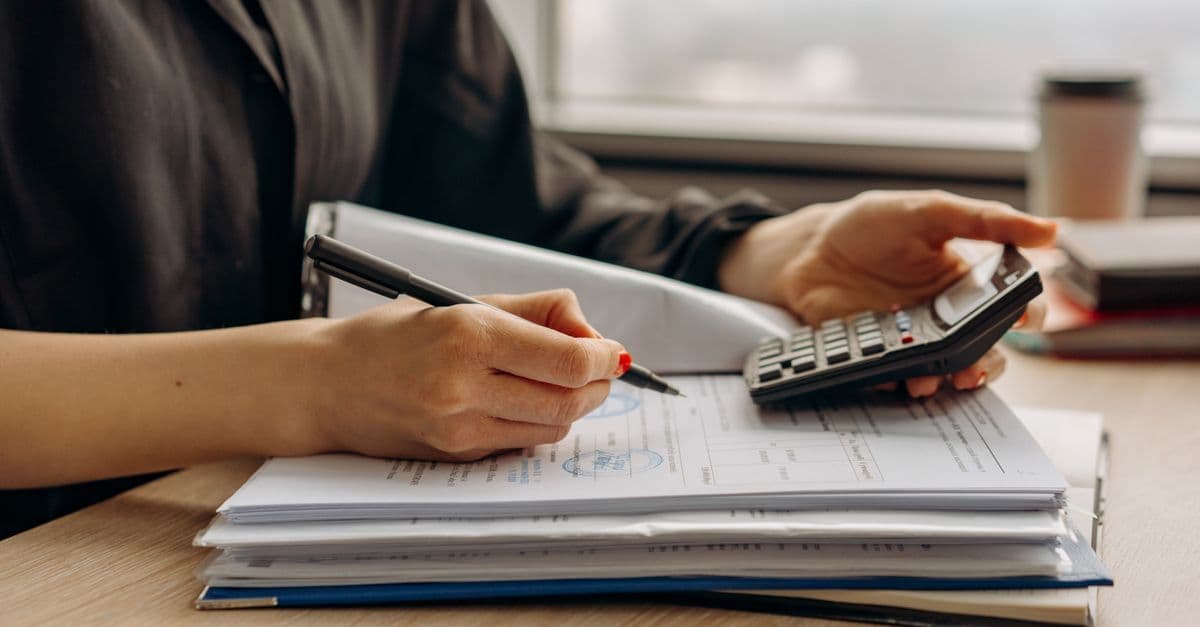 Person bedient einen Taschenrechner über Finanzunterlagen im Büro.