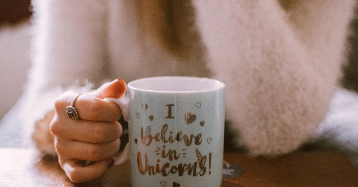 Hand holding a unicorn-themed mug with a cozy and warm vibe, perfect for morning coffee or tea.
