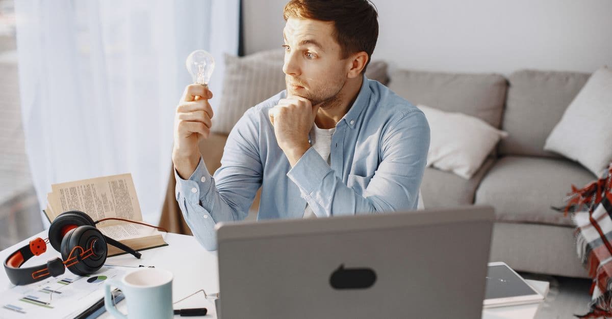 Young man at home desk holding a lightbulb, symbolizing a moment of inspiration during remote work.
