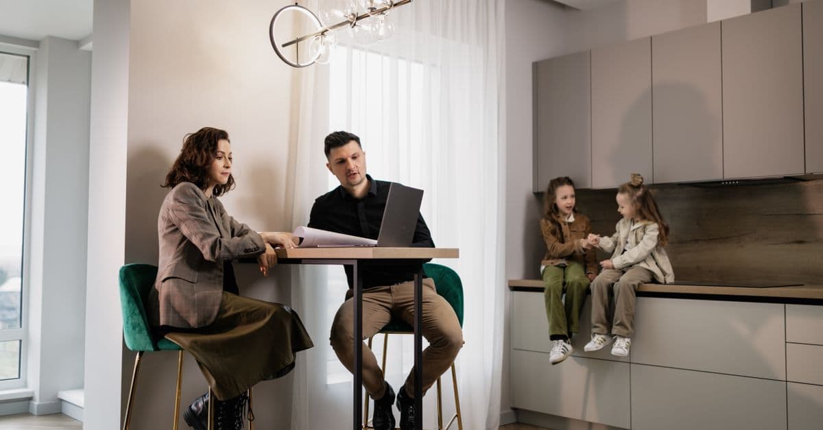 Familie sitzt gemeinsam in einer modernen Küche und schaut zusammen auf einen Laptop.
